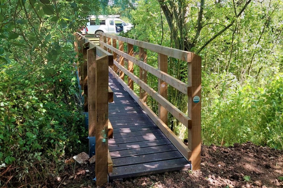 A foot bridge constructed from timber parapets, recycled plastic deck boards and galvanised steel beams